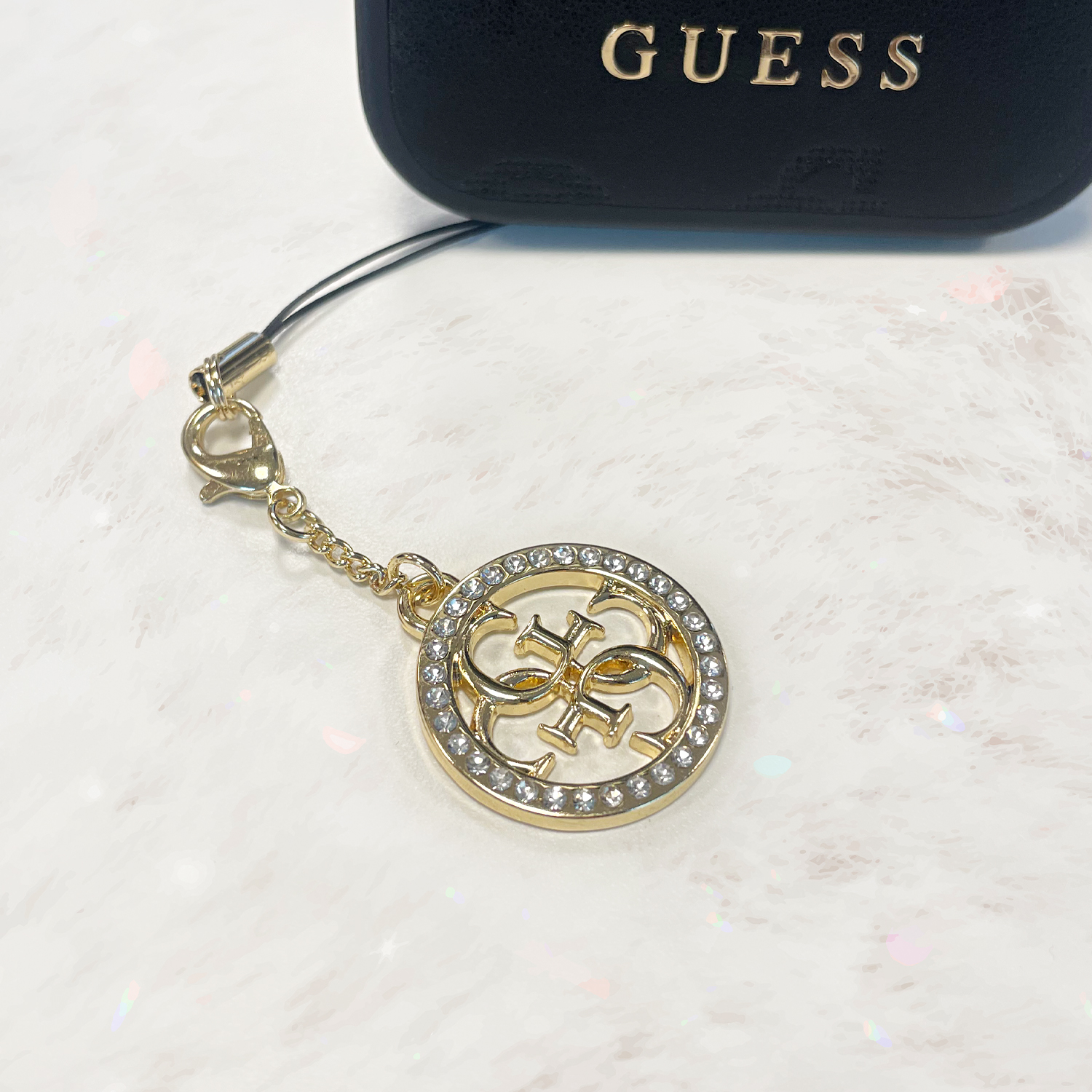 Zawieszka Guess GUCPM4DRD Phone Strap 4G, złota. Elegancki dodatek z Kamieniami Rhinestone.